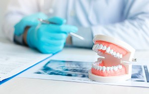 Dentist’s gloved hands leaning at desk with model teeth, X-rays, and treatment plan
