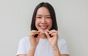 Woman smiling while holding clear aligner