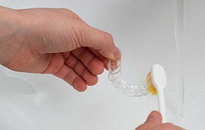 Patient cleaning clear aligner in sink