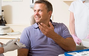 Smiling man talking to dentist about full mouth rehabilitation in dental chair