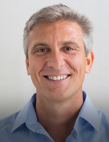 Older man in light blue collared shirt smiling