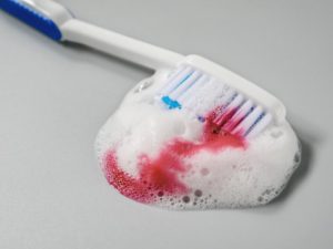 Toothbrush with white foam and blood on gray background