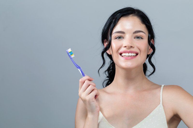 Smiling woman holding a toothbrush against gray background