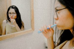 Woman brushing her teeth and looking in the bathroom mirror.
