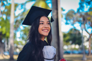 Smiling young woman in black graduation cap and gown