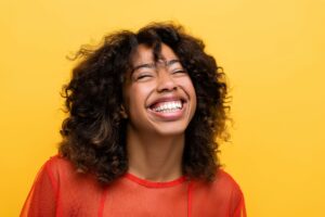 Woman with brown hair smiling with yellow background