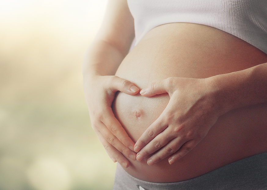 Woman holding pregnant belly with hands in heart shape